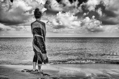 Rear view of woman standing at beach against sky