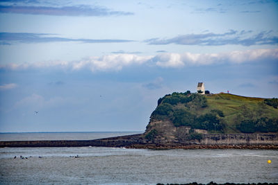 Lighthouse on beach by sea against sky