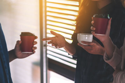 Midsection of people holding disposable coffee cup while discussing in office