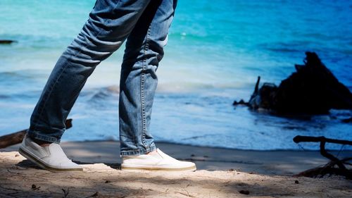 Low section of man walking on shore at beach