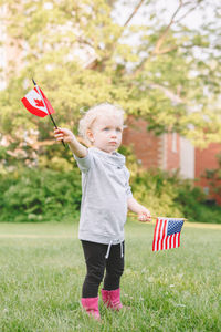 Girl holding american and canadian flag while standing on grass