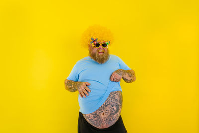 Young man wearing sunglasses standing against yellow background