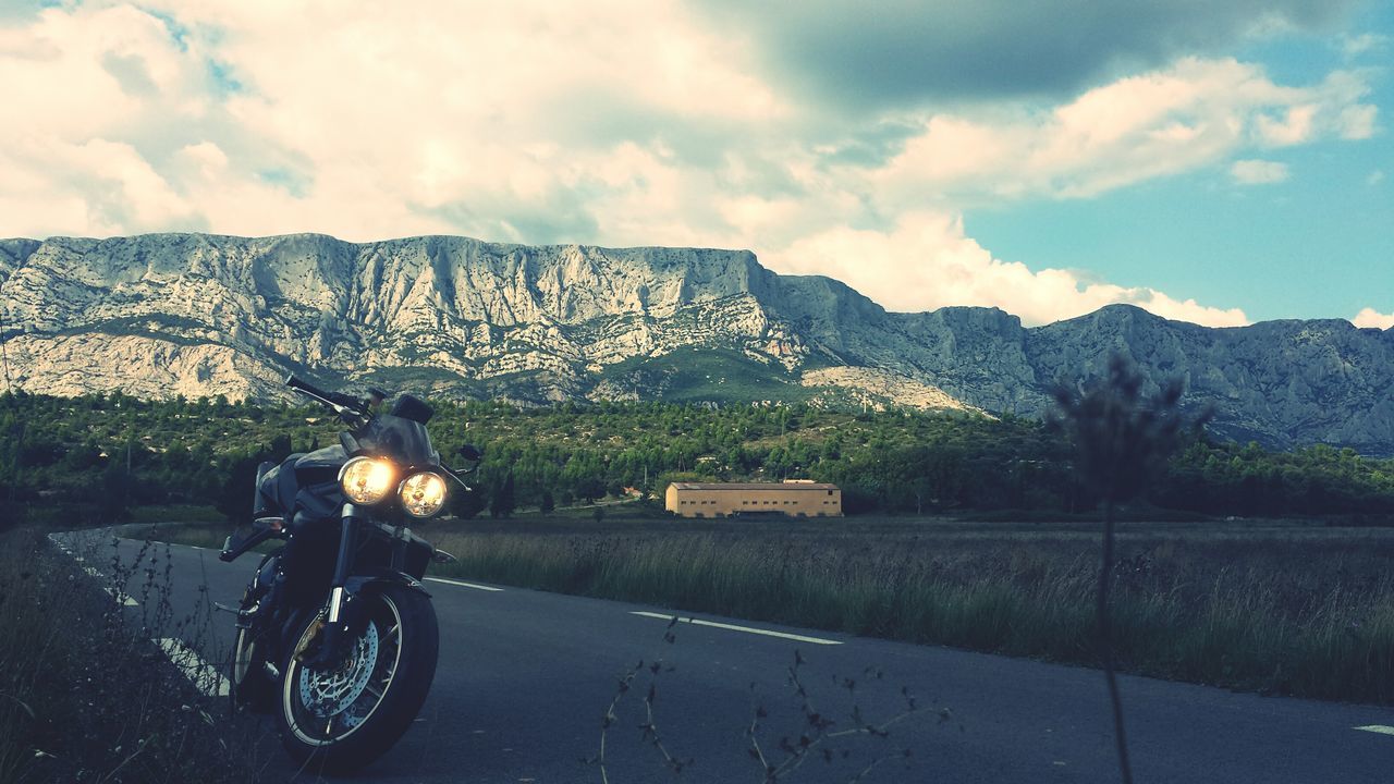 transportation, land vehicle, mountain, sky, road, mode of transport, bicycle, cloud - sky, mountain range, landscape, lifestyles, men, riding, car, full length, street, cloud, tree