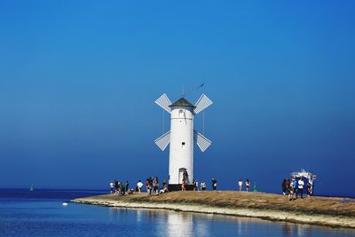 People on lighthouse by sea against clear blue sky