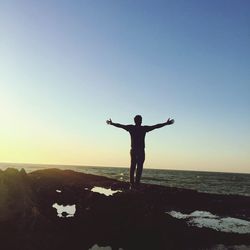 Rear view of man standing with arms outstretched on rock against sky