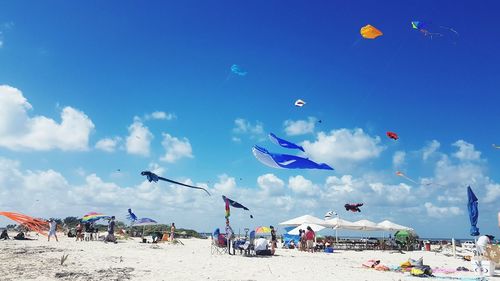 People flying kites at beach against blue sky