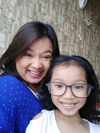 Portrait of smiling mother and daughter sitting against wall