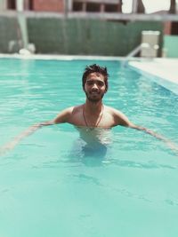 Portrait of shirtless man swimming in pool during sunny day