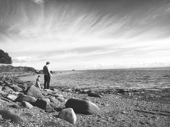 Father and son standing at sea shore against sky