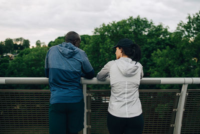 Rear view of male and female athletes talking while leaning on railing on footbridge