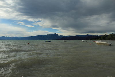 Boats in sea against cloudy sky