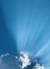 Low angle view of sunlight streaming through clouds