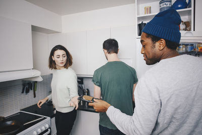 Man giving food package to female roommate in kitchen at college dorm