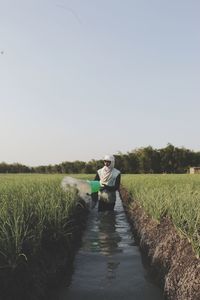 Farmer watering crops on agricultural field against sky