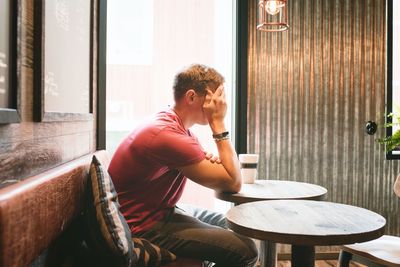 Man sat covering his face looking stressed whilst in a cafe drinking