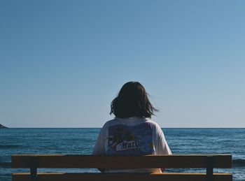 Rear view of woman sitting on bench against clear sky