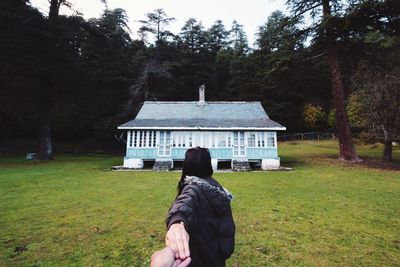 Rear view of woman walking on grassland against built structure