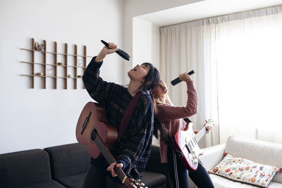 Playful friends holding combs and guitars singing together at home