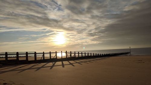 Pier on beach against sky during sunset