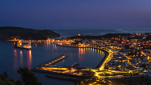 High angle view of illuminated buildings by sea against sky at night