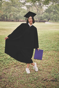 Young woman in graduation gown standing on field