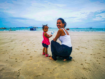 Rear view of women with baby girl on beach against sea