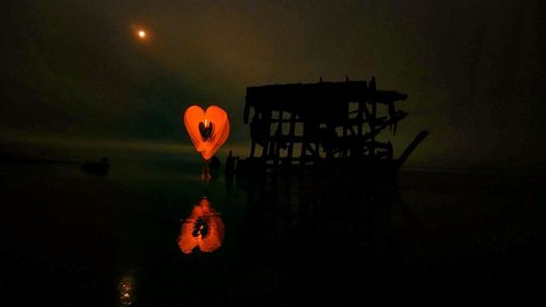 Silhouette of illuminated orange light against sky at night