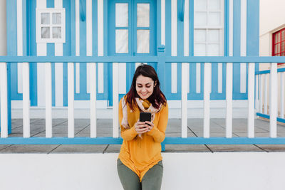 Happy woman using mobile phone in front of colorful houses.costa nova, aveiro, portugal