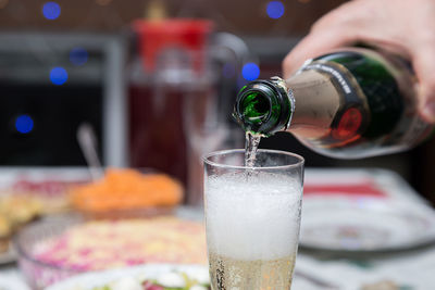 Close-up of hand pouring drink in champagne flute at table