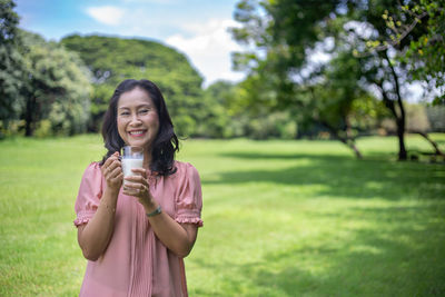 Portrait of smiling woman holding milk in glass on field
