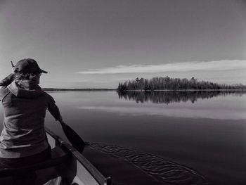 Rear view of person paddling in canoe against sky on sunny day