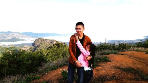 Siblings standing on mountain against sky