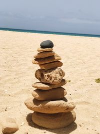 Stack of pebbles on sand at beach against sky