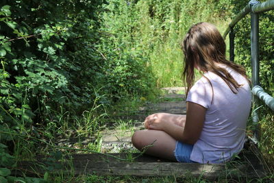 Side view of woman sitting on land in forest