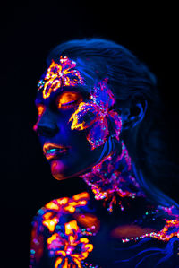 Close-up of woman with illuminated body paint against black background