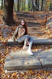 Full length of young woman sitting on tree trunk