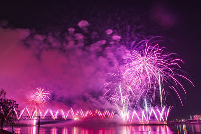 Illuminated firework display over river at night