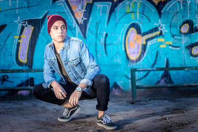 Portrait of young man looking away while sitting on wall