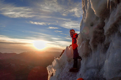 Man standing on snow covered rock against sky during sunset