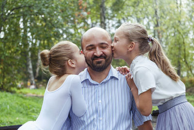 Two daughters with care and gratitude kiss dad on the cheeks and he smiles with happiness 