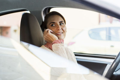 Smiling businesswoman looking away while using smart phone in car