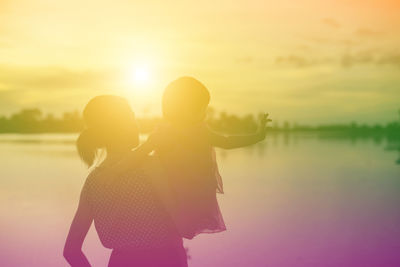 Rear view of women standing against sky during sunset