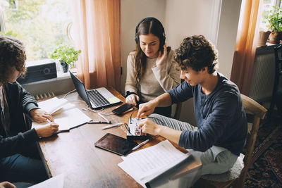 High angle view of friends using sound mixer while teenage boy studying at table in room