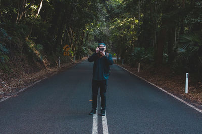 Man photographing with camera on street amidst trees in forest