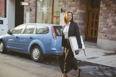 Female realtor carrying signboard and bag while walking on street in city