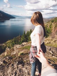 Cropped image of man holding woman hand on mountain against lake