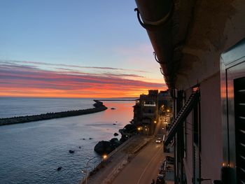 Illuminated city by sea against sky during sunset