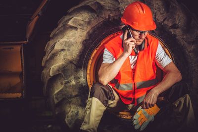 Male worker talking on mobile phone while sitting over tire