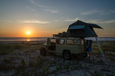 Tent on vehicle at beach against sky during sunset