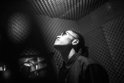 Young man wearing sunglasses looking up while standing indoors